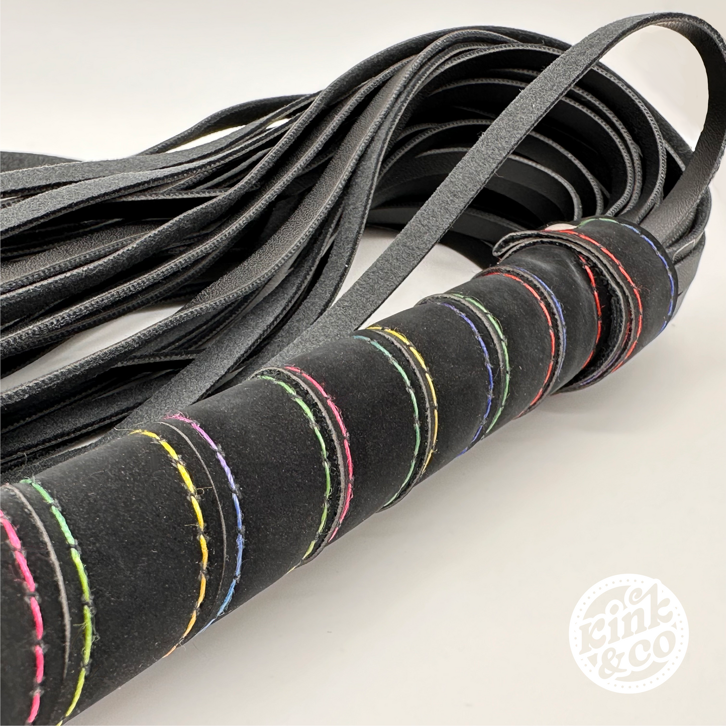 Close up of the rainbow stitching on the handle of black flogging whip with kink and co logo in bottom right of image