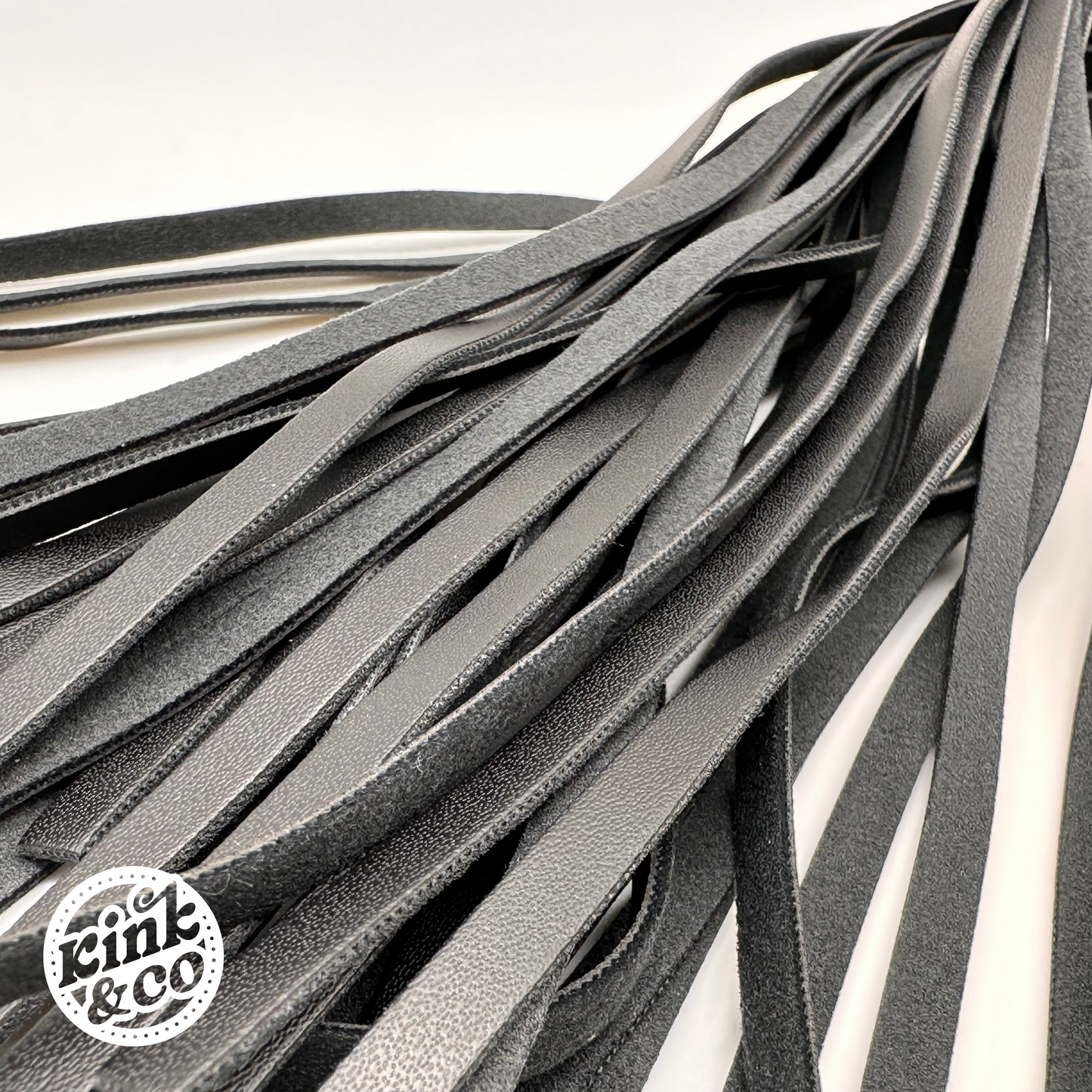 Close up of the whip end. Black faux leather BDSM flogging whip with rainbow stitching spiral on the handle. Grey background with kink and co logo in the top left
